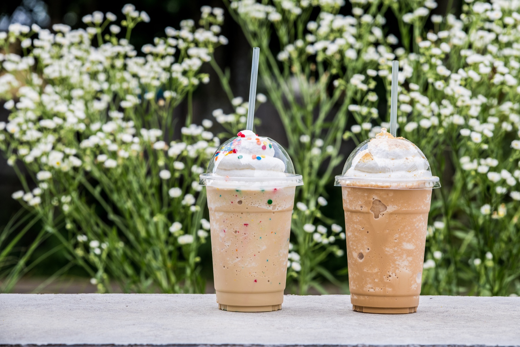 Two cold coffee drinks in front of summer flowers